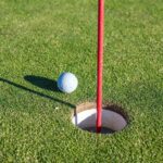 Golf ball beside a red flagstick and hole on a putting green
