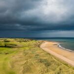 Coastal links golf course beside a beach beneath dark storm clouds