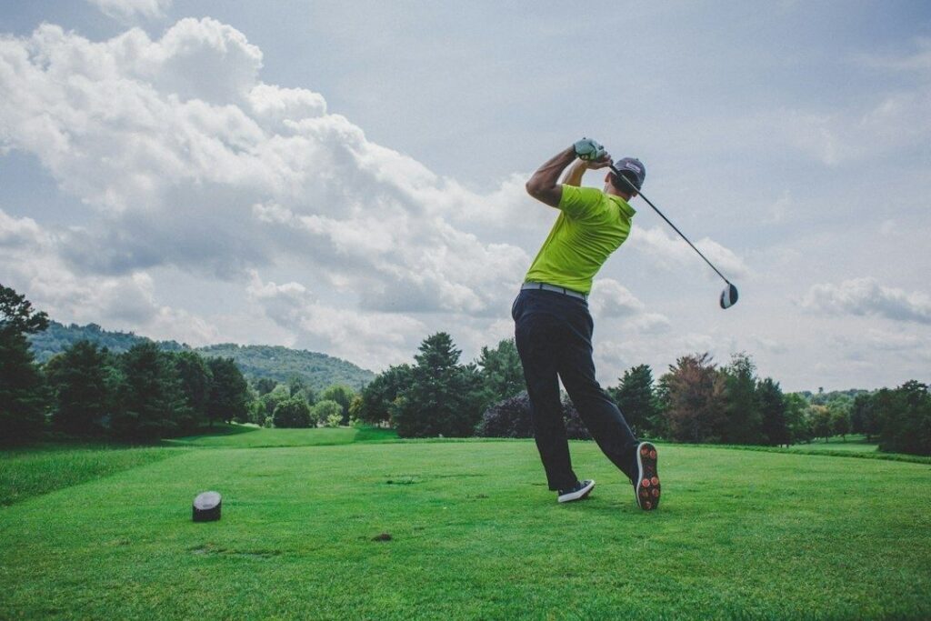 Golfer completing a tee-shot swing on a course under cloudy skies