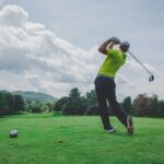Golfer completing a tee-shot swing on a course under cloudy skies